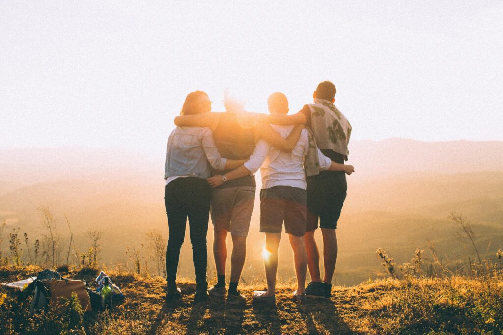 Four friends embracing one another on top of a mountain at sunset.