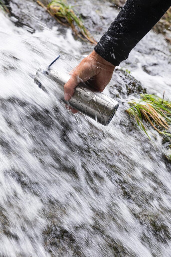 Person filling up a metal water bottle from a fresh waterfall.