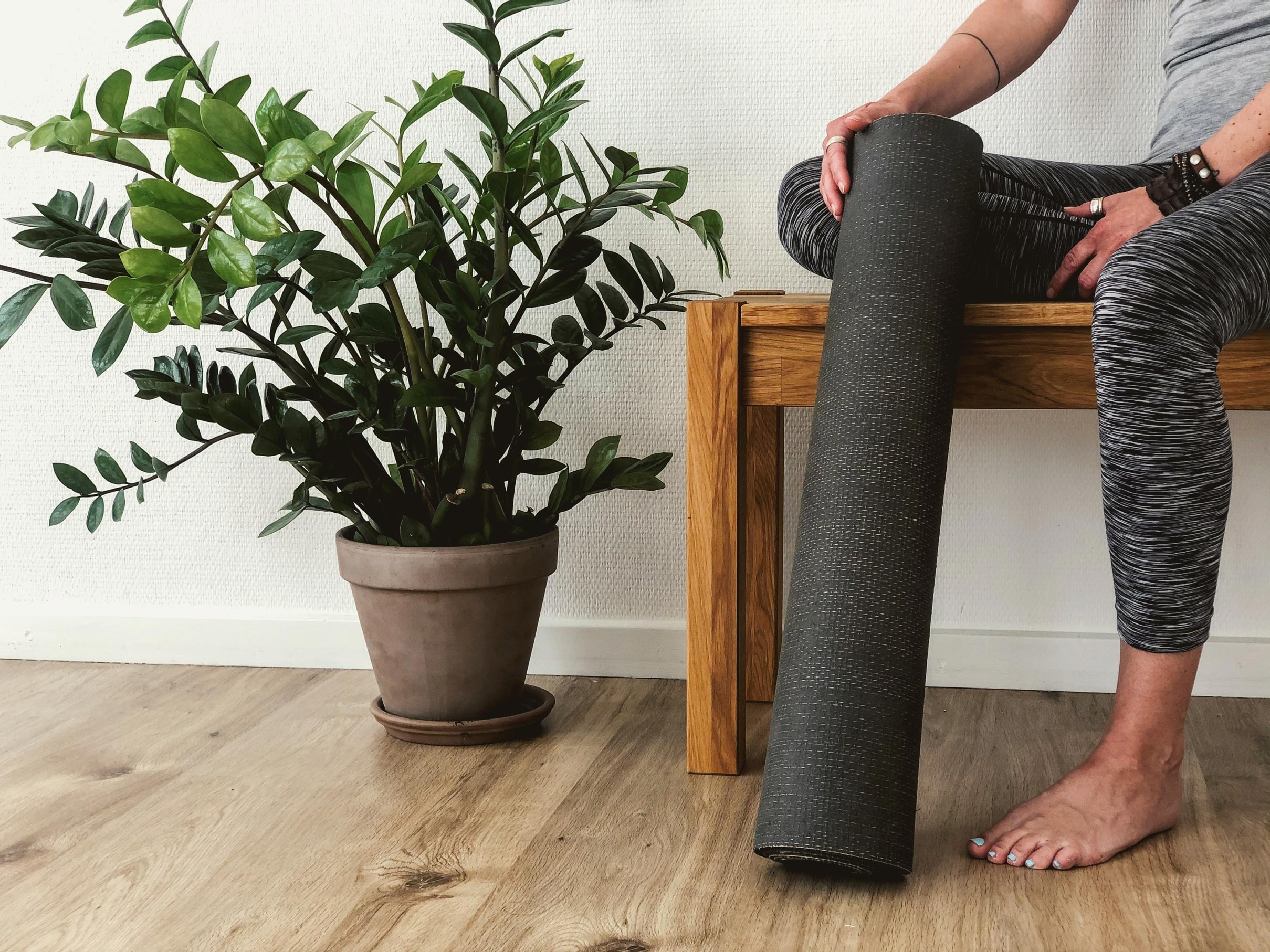 Woman sitting on a wooden bench with yoga mat next to a plant pot.